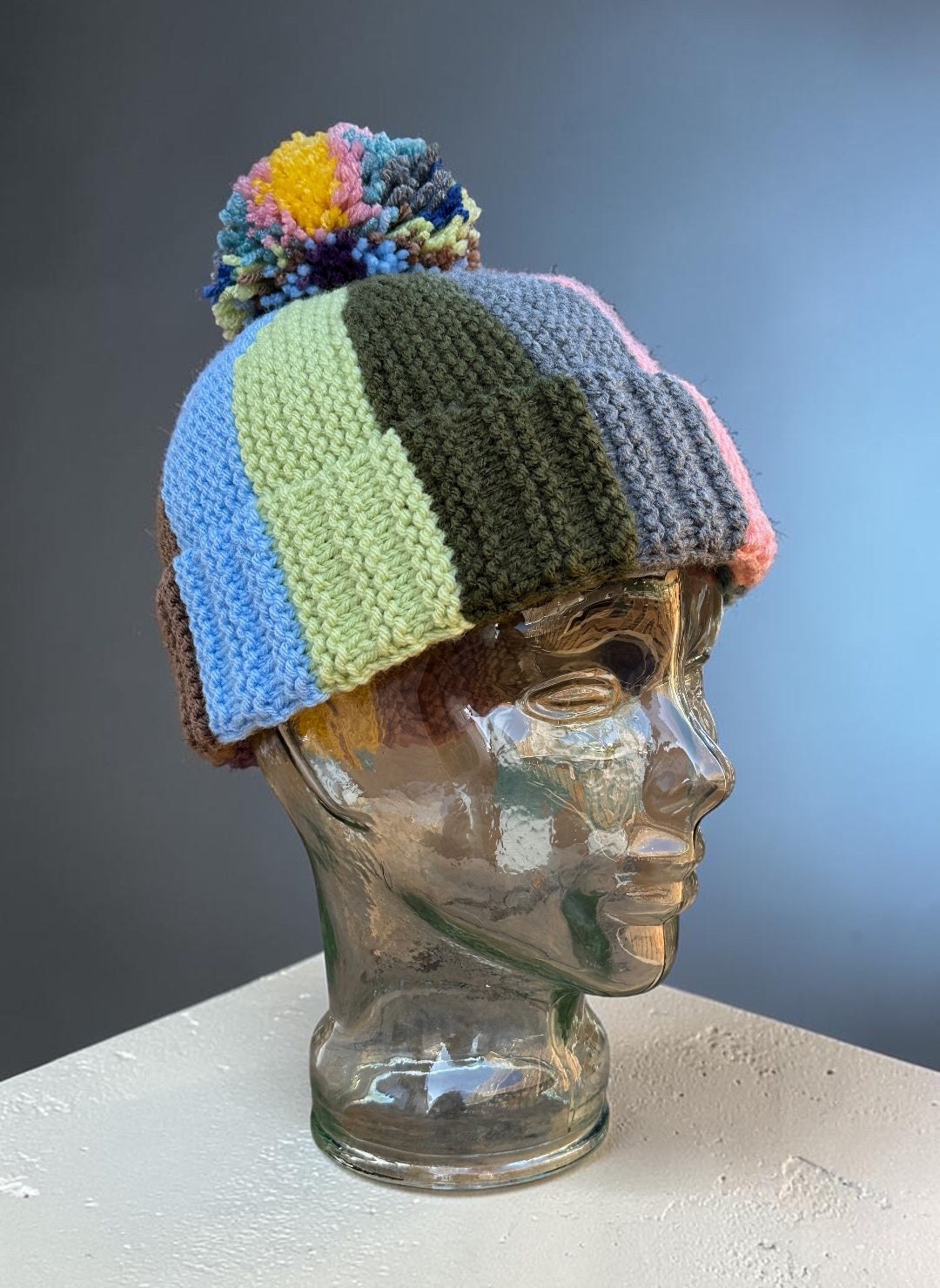Colorful striped knit hat on a mannequin head against a gradient background