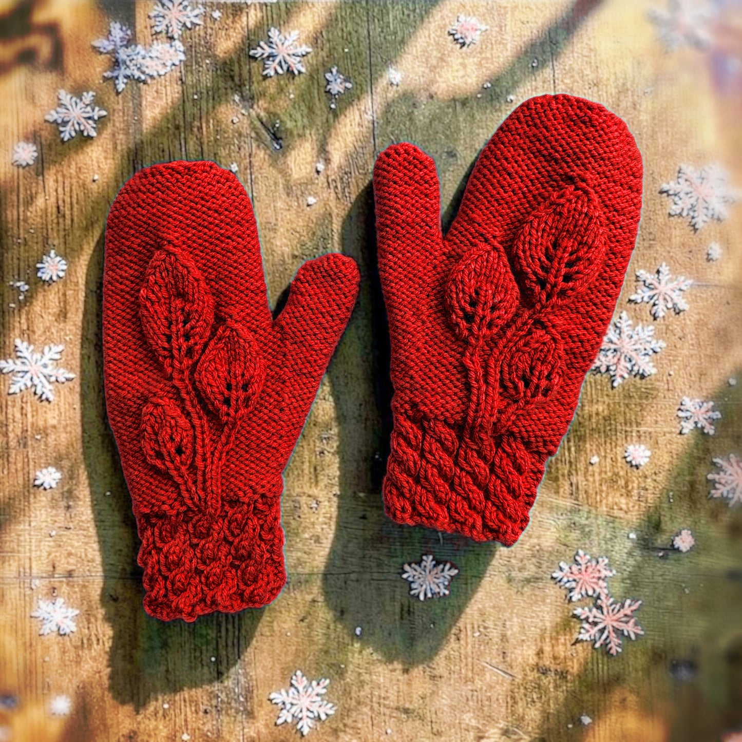 Red knitted mittens on a wooden surface with decorative snowflakes.