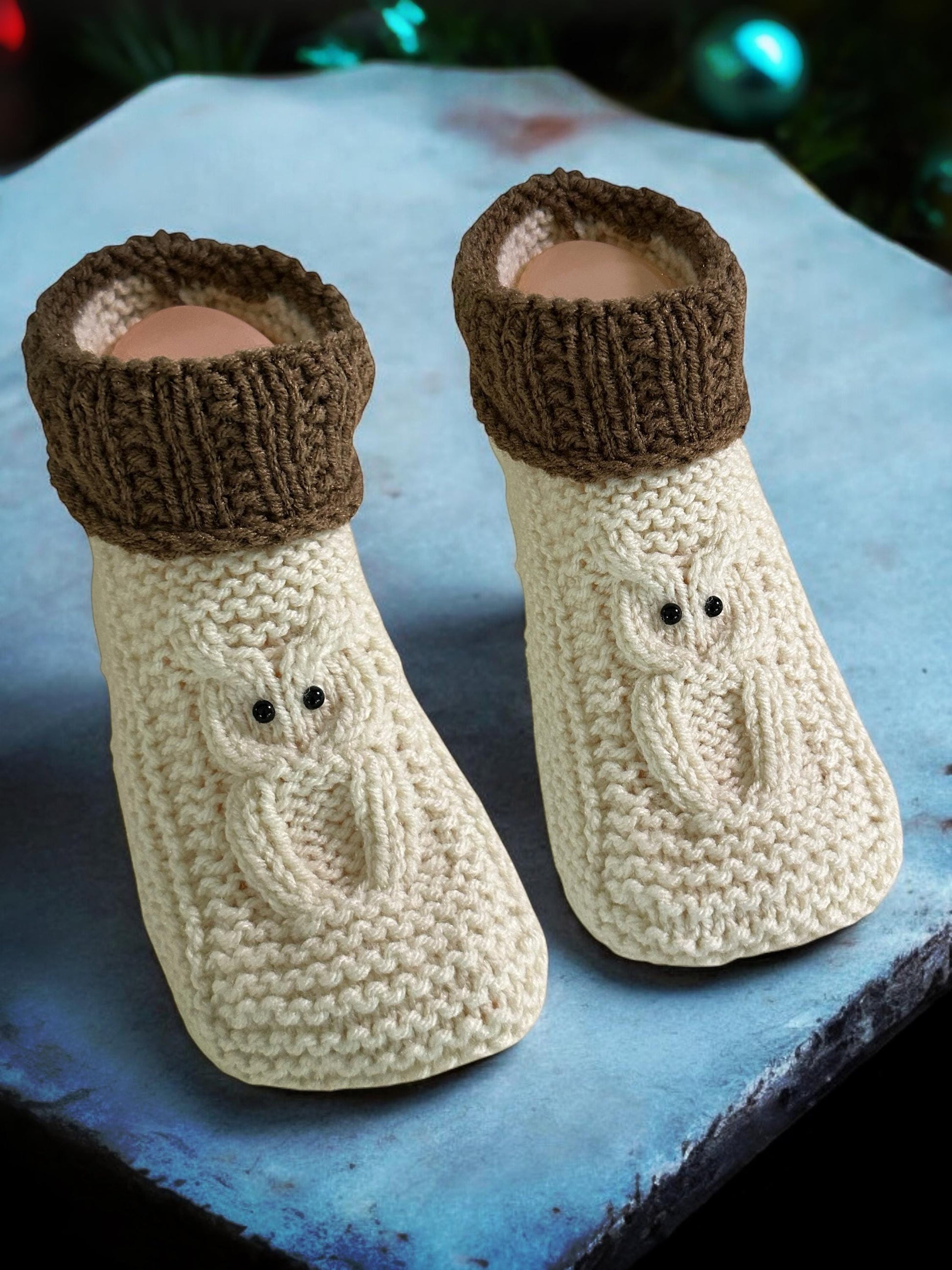 A pair of knitted cable owl slippers with a cuff, displayed on a blue surface.