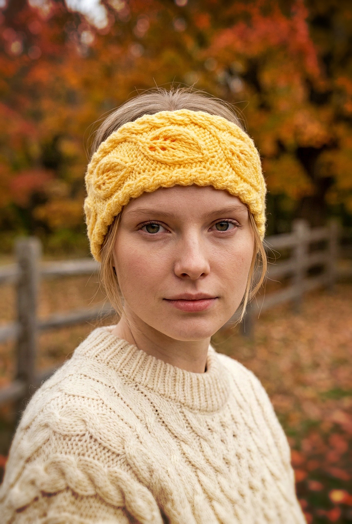 Woman wearing a yellow knitted headband and beige sweater in an autumn setting.