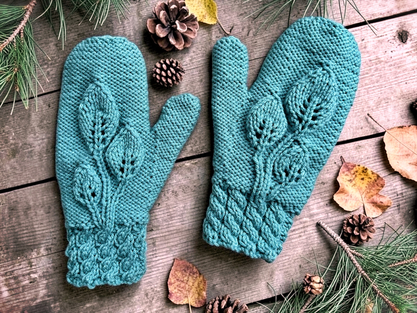 Pair of teal knitted mittens on a wooden surface with pine cones and leaves. knitting pattern