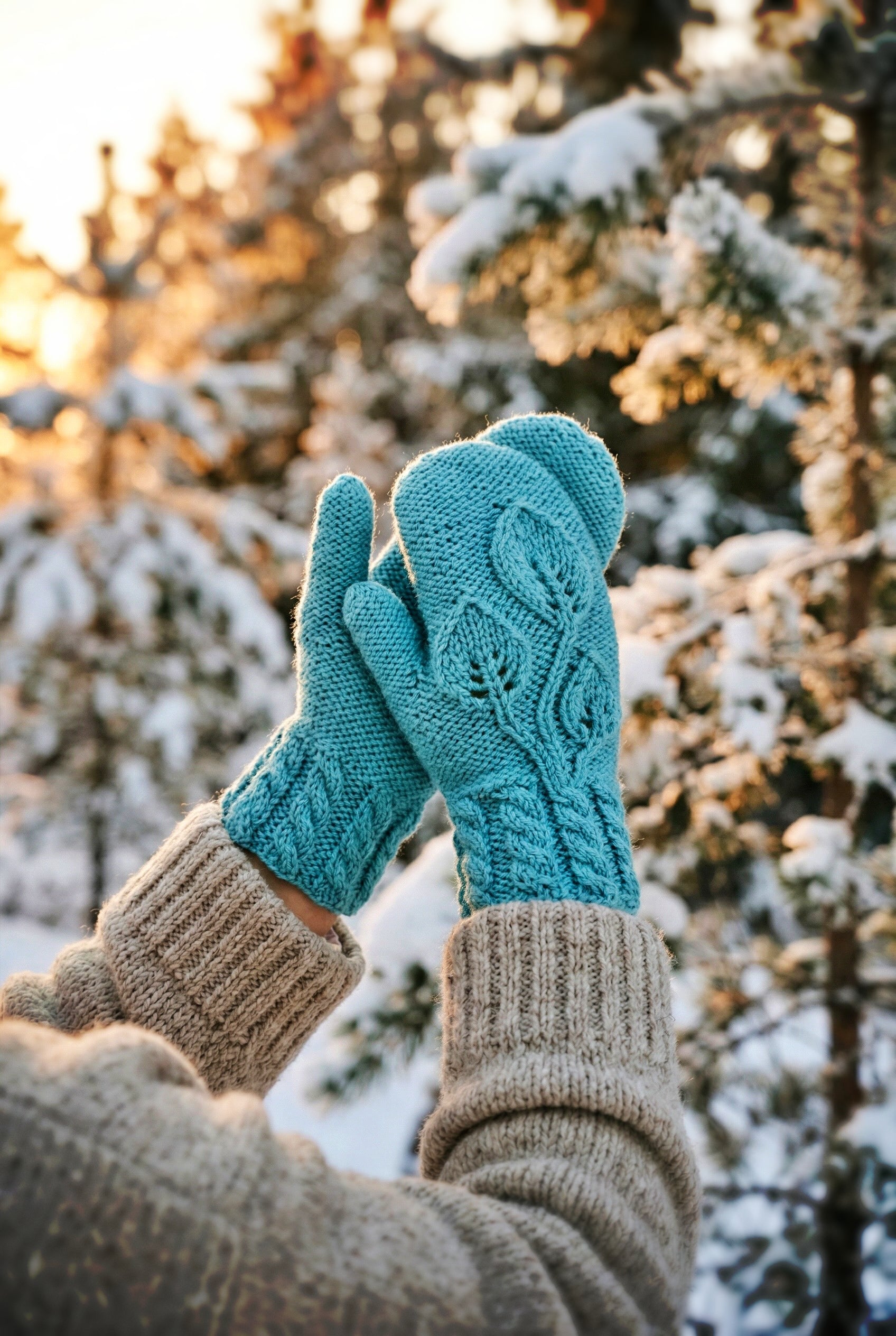 Teal mittens held against a snowy forest background knitting pattern