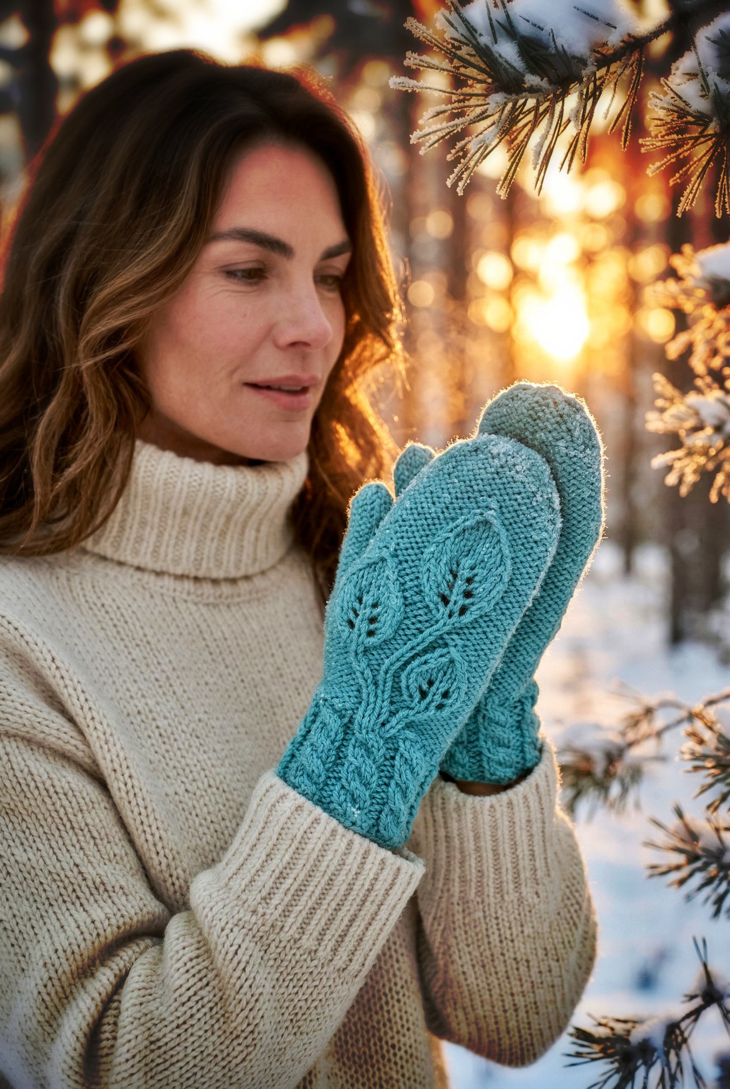 Woman wearing a beige sweater and blue mittens in a snowy forest with a sunset.
