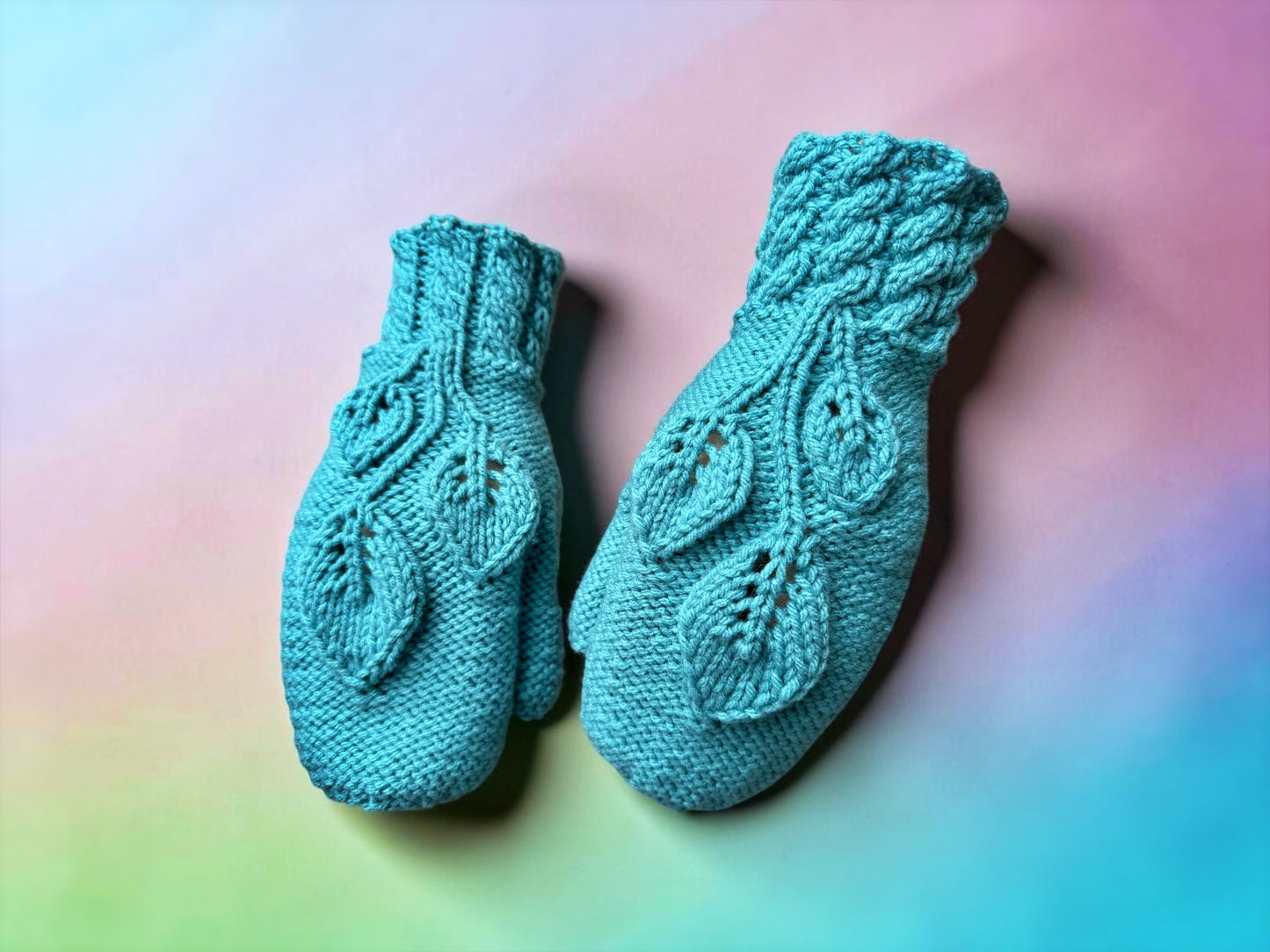 Pair of teal knitted mittens on a colorful background knitting pattern