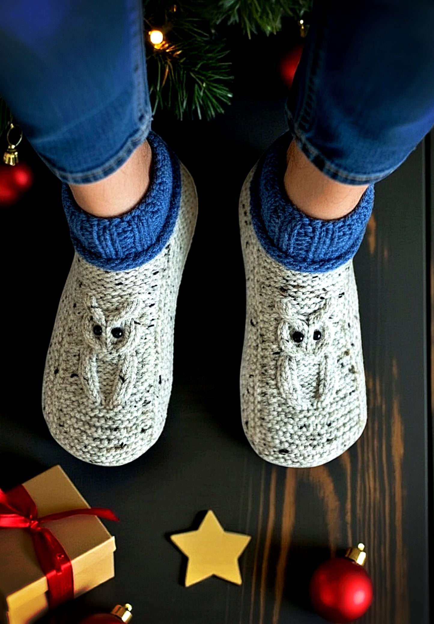Person wearing owl-patterned slippers on a dark surface with Christmas decorations.