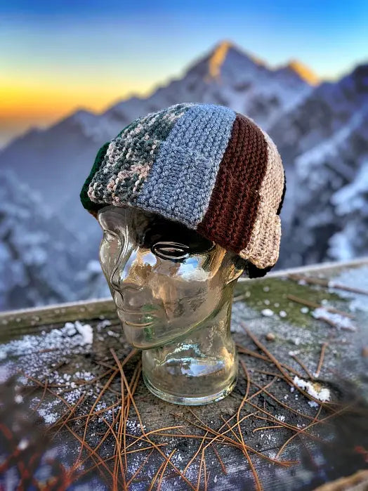 Knitted multicolored beanie on a glass mannequin head with a mountainous landscape in the background