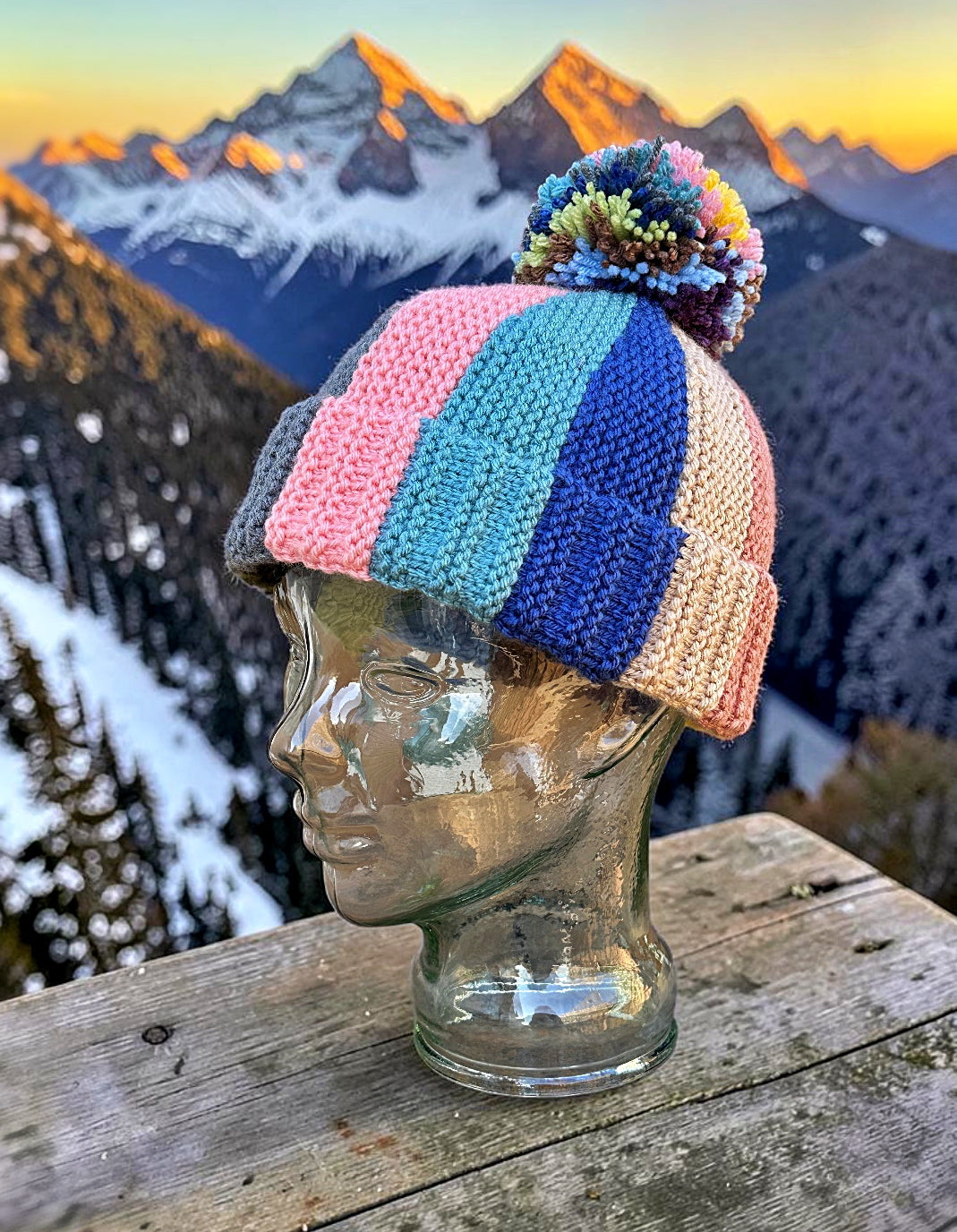 Colorful knitted beanie on a mannequin head with a mountainous landscape in the background