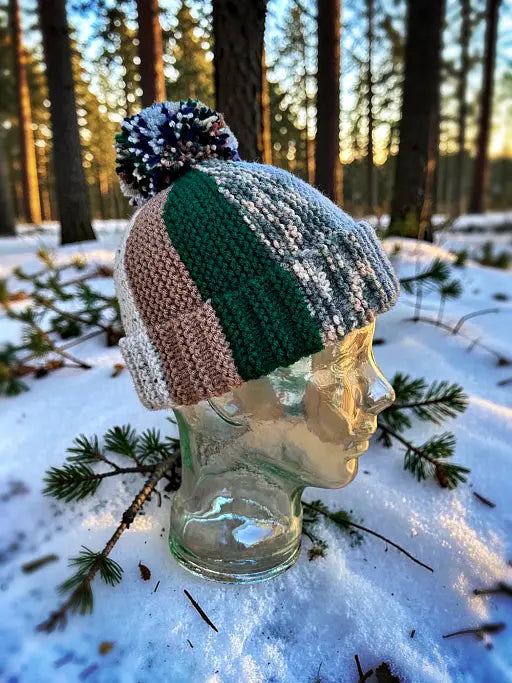 Knitted beanie with a pom-pom on a glass mannequin head in a snowy forest setting
